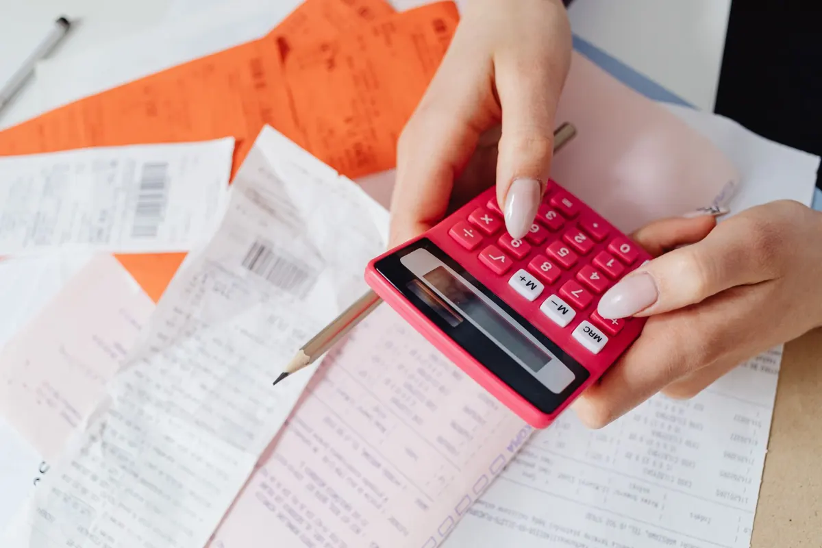 Hands adding up receipts on a pink calculator