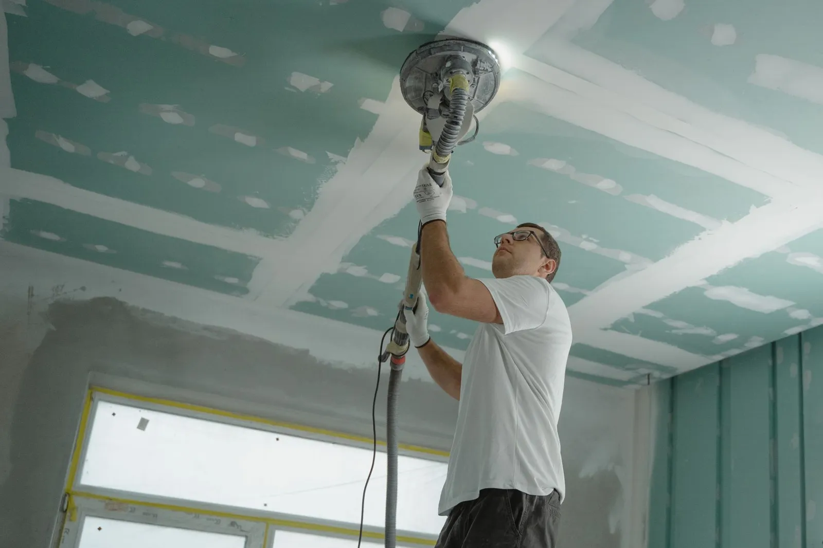 Contractor sanding a new drywall ceiling in a home renovation