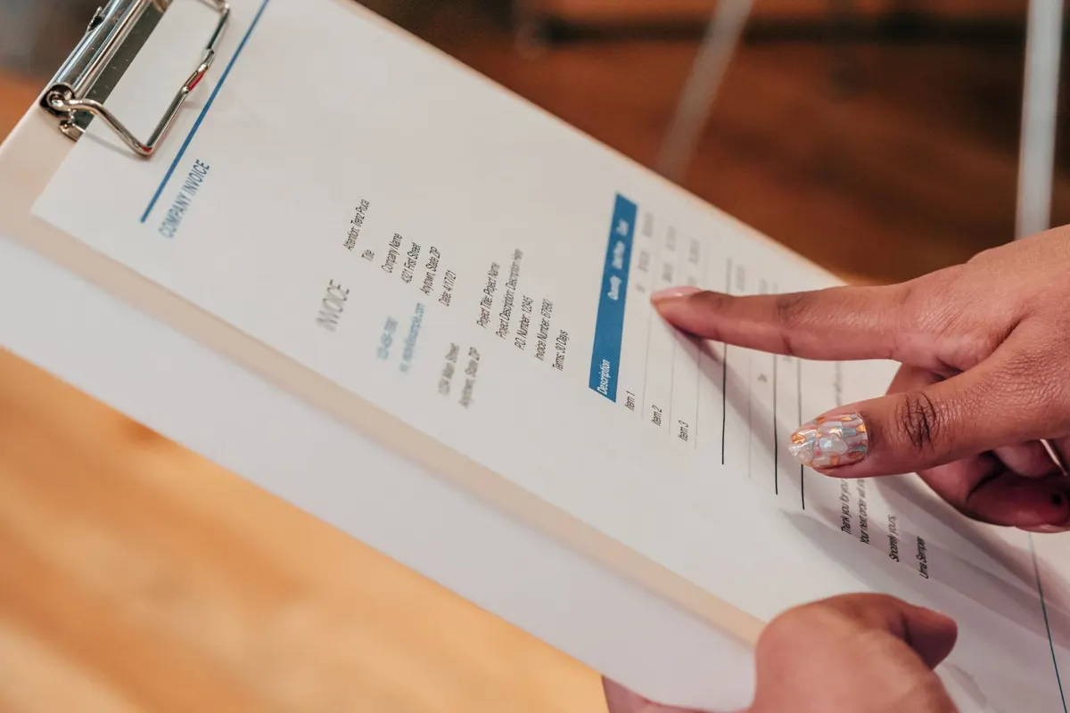 A finger pointing at a line on a clipboard invoice