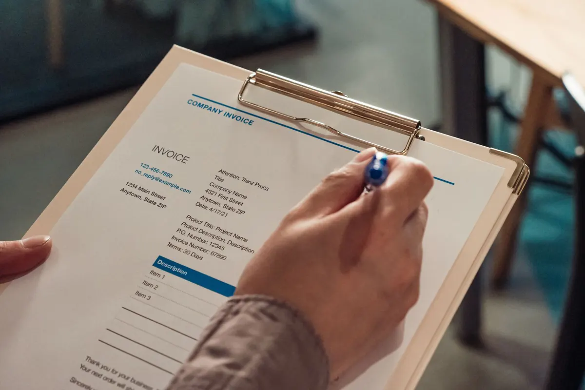A hand filling in an invoice on a clipboard