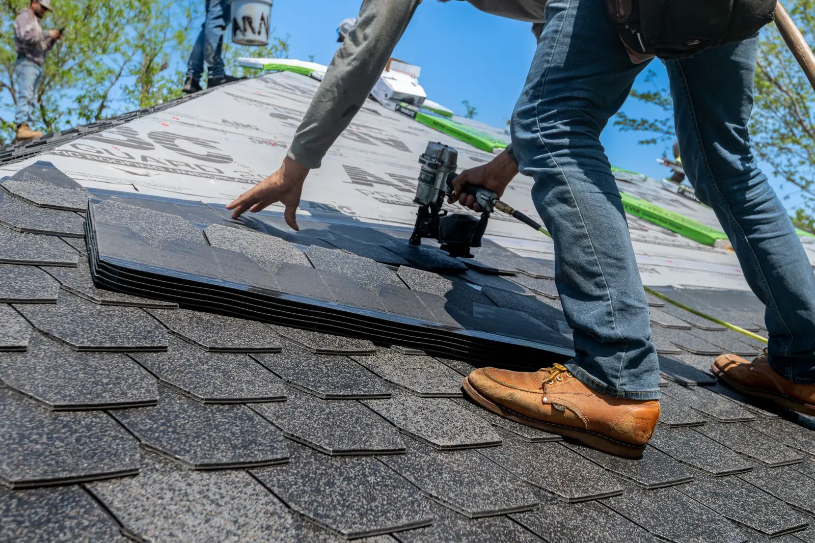 Roofer nailing new asphalt shingles on a house