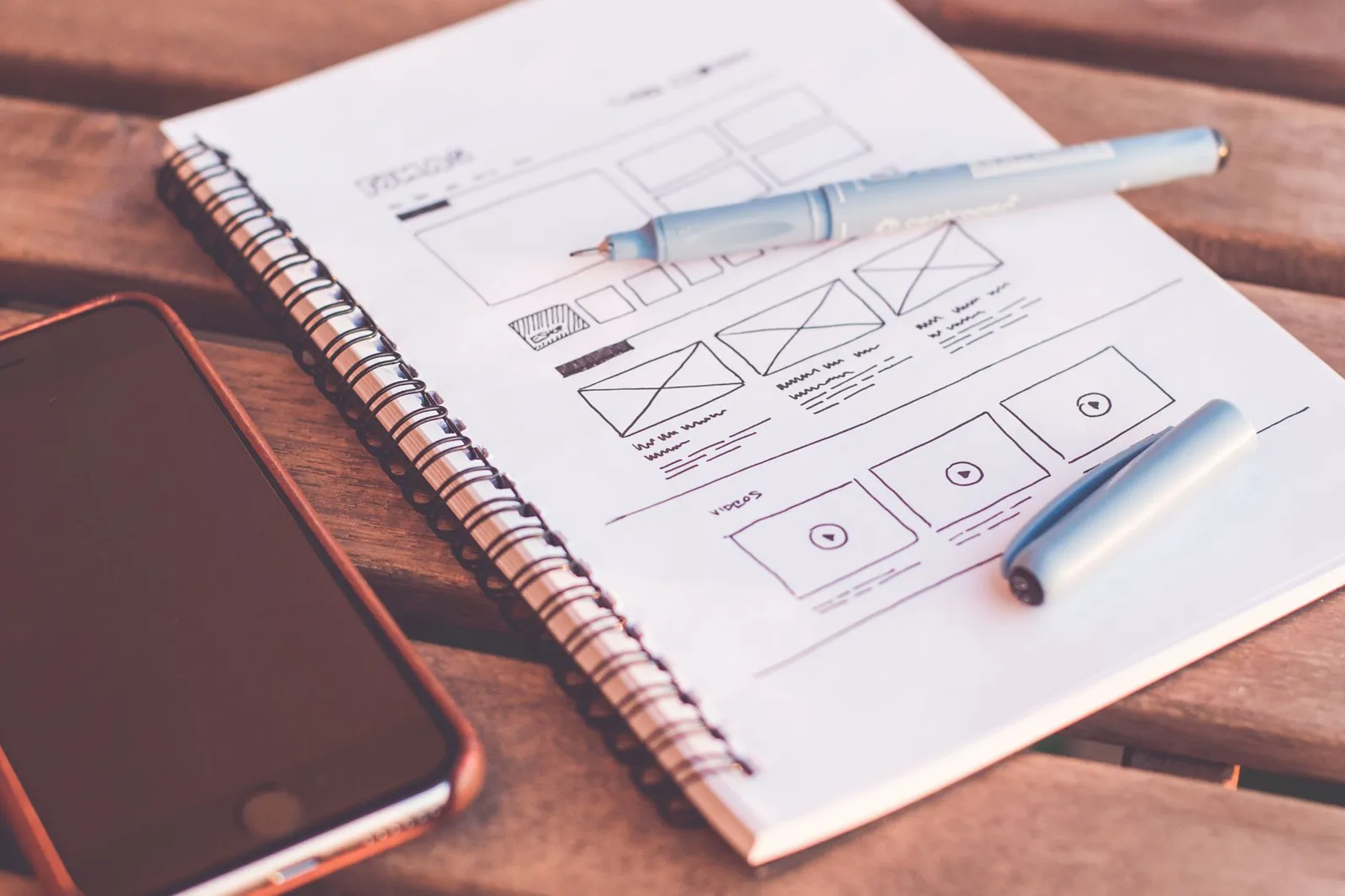 Hand-drawn website page layout in a notebook next to a phone